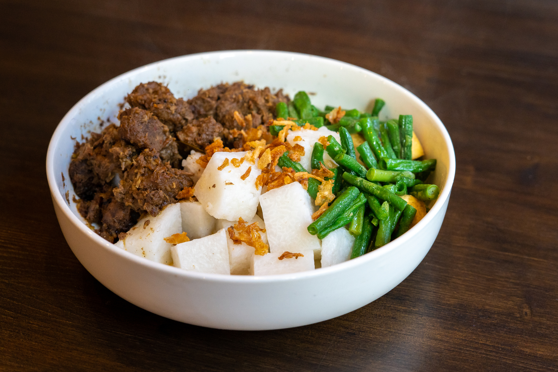 A plate of Javanese food with beef rendang , lontong rice and green beans