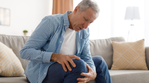 Mature man with knee pain sitting on couch at home