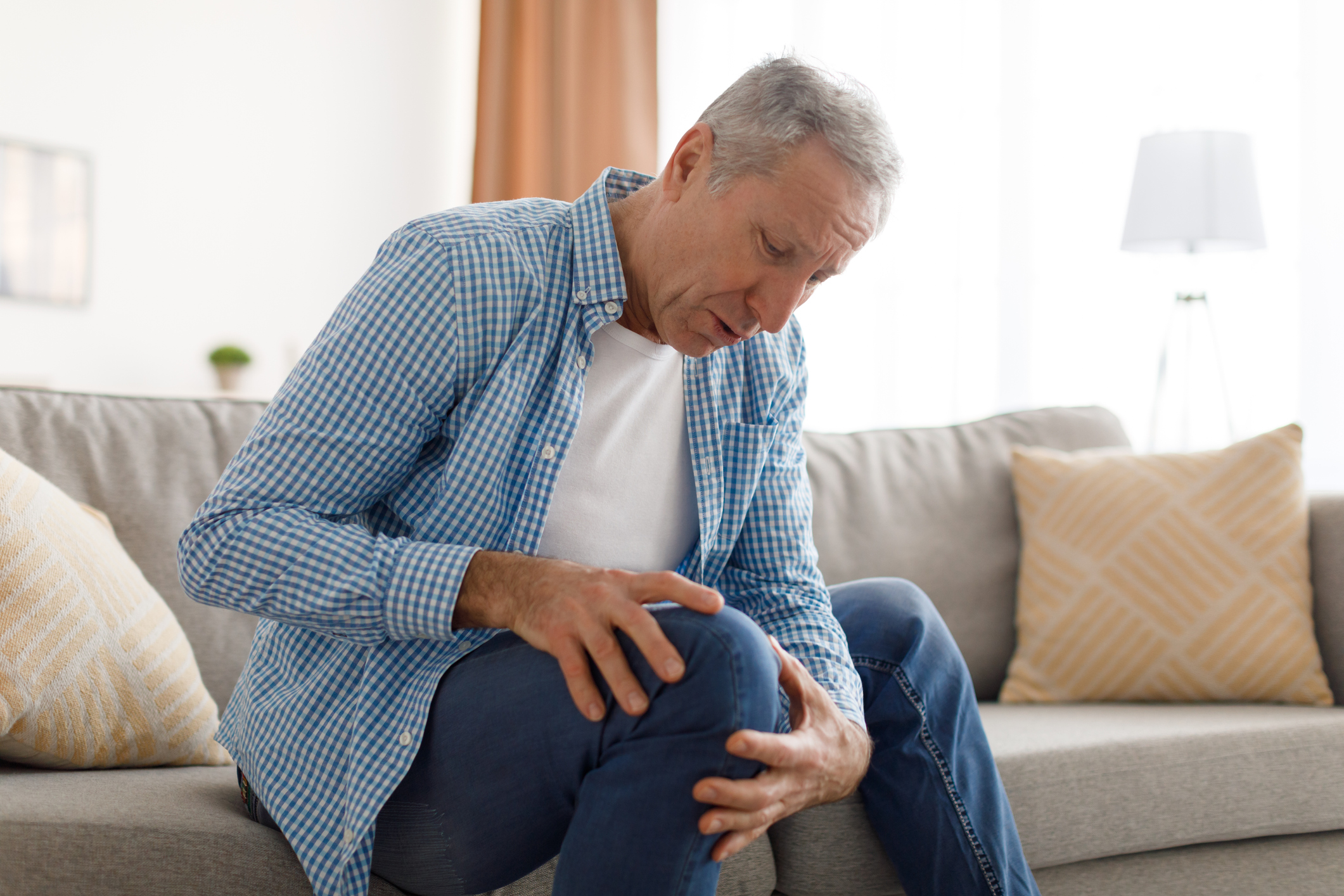 Mature man with knee pain sitting on couch at home