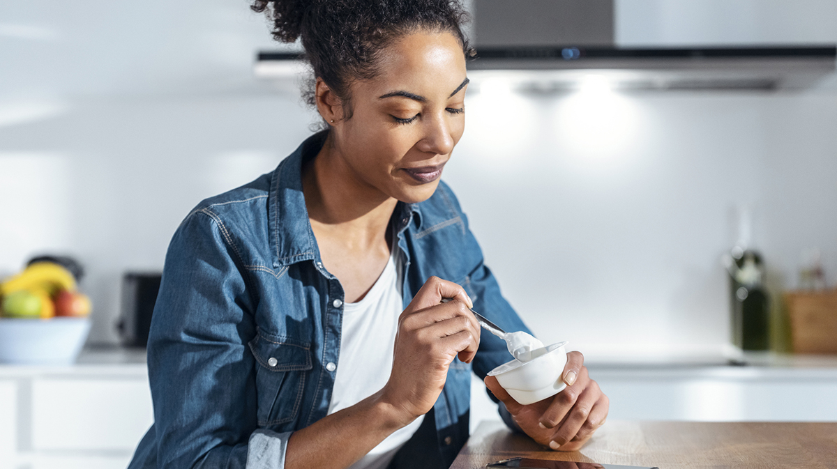Woman eating yogurt sitting in kitchen at home