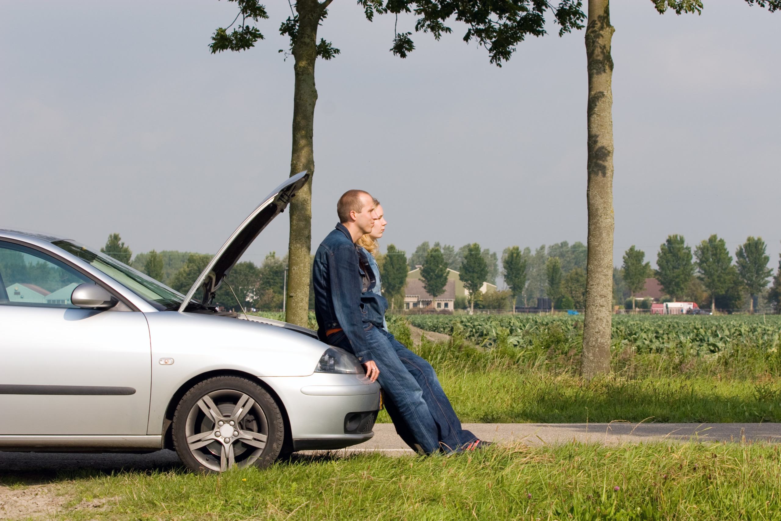 Two people leaning against the open hood of a car outdoors