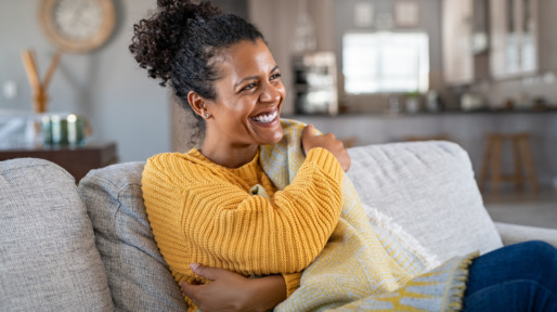Joyful african woman with blanket on couch laughing