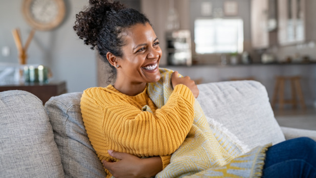 Joyful african woman with blanket on couch laughing