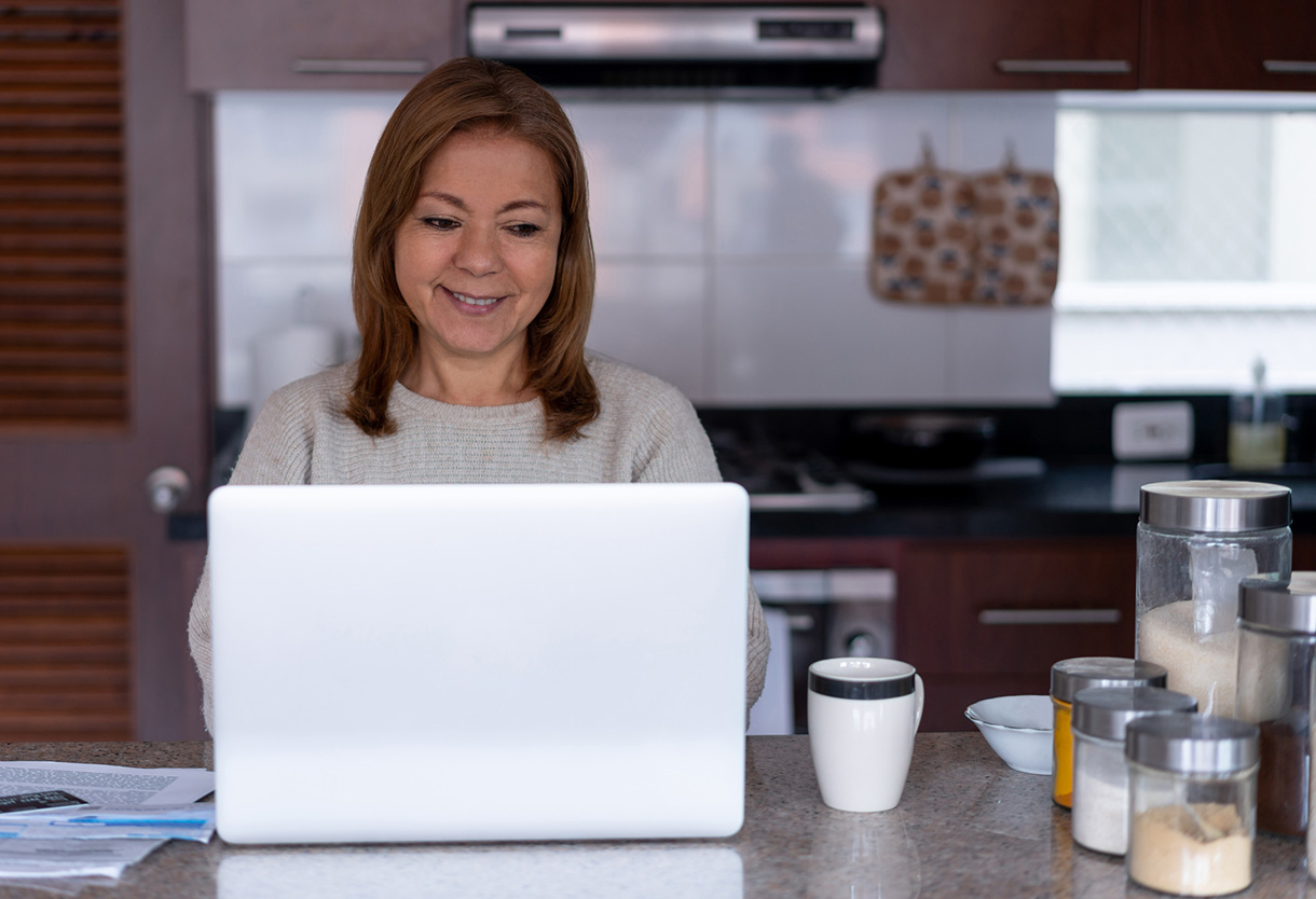 Happy Latin American mature woman working from home using her laptop very cheerfully and smiling