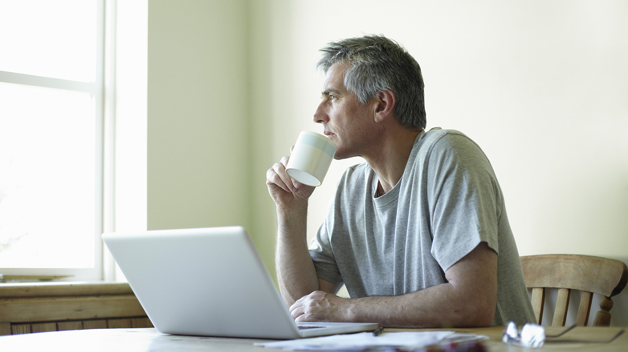 Man with laptop and coffee looking out of window