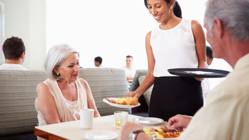 Waitress Serving Senior Couple Breakfast In Hotel Restaurant