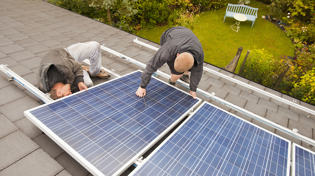 Technicians fitting solar photo voltaic panels to a house roof in Ambleside, Cumbria, UK.
