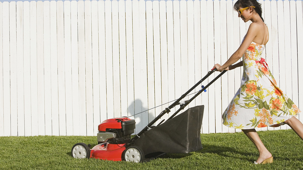 Hispanic woman in dress pushing lawn mower