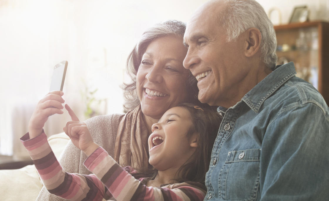 Grandparents and granddaughter taking selfie on sofa