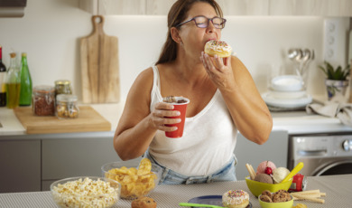 Ultra processed foods zoals chips, donuts, frisdrank, koek en ijs. Vrouw smult van sterk bewerkt voedsel