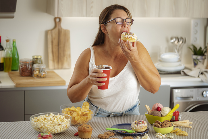 Ultra processed foods zoals chips, donuts, frisdrank, koek en ijs. Vrouw smult van sterk bewerkt voedsel