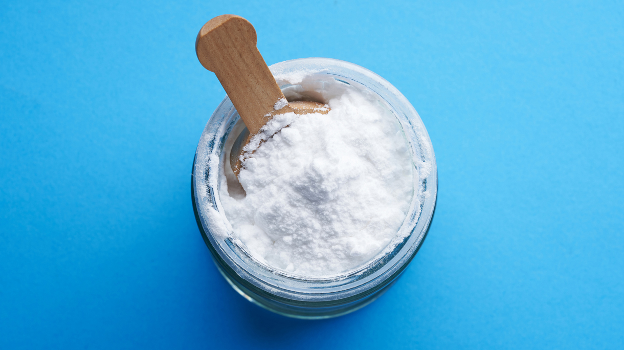 Een glazen potje met baking soda op een blauwe achtergrond