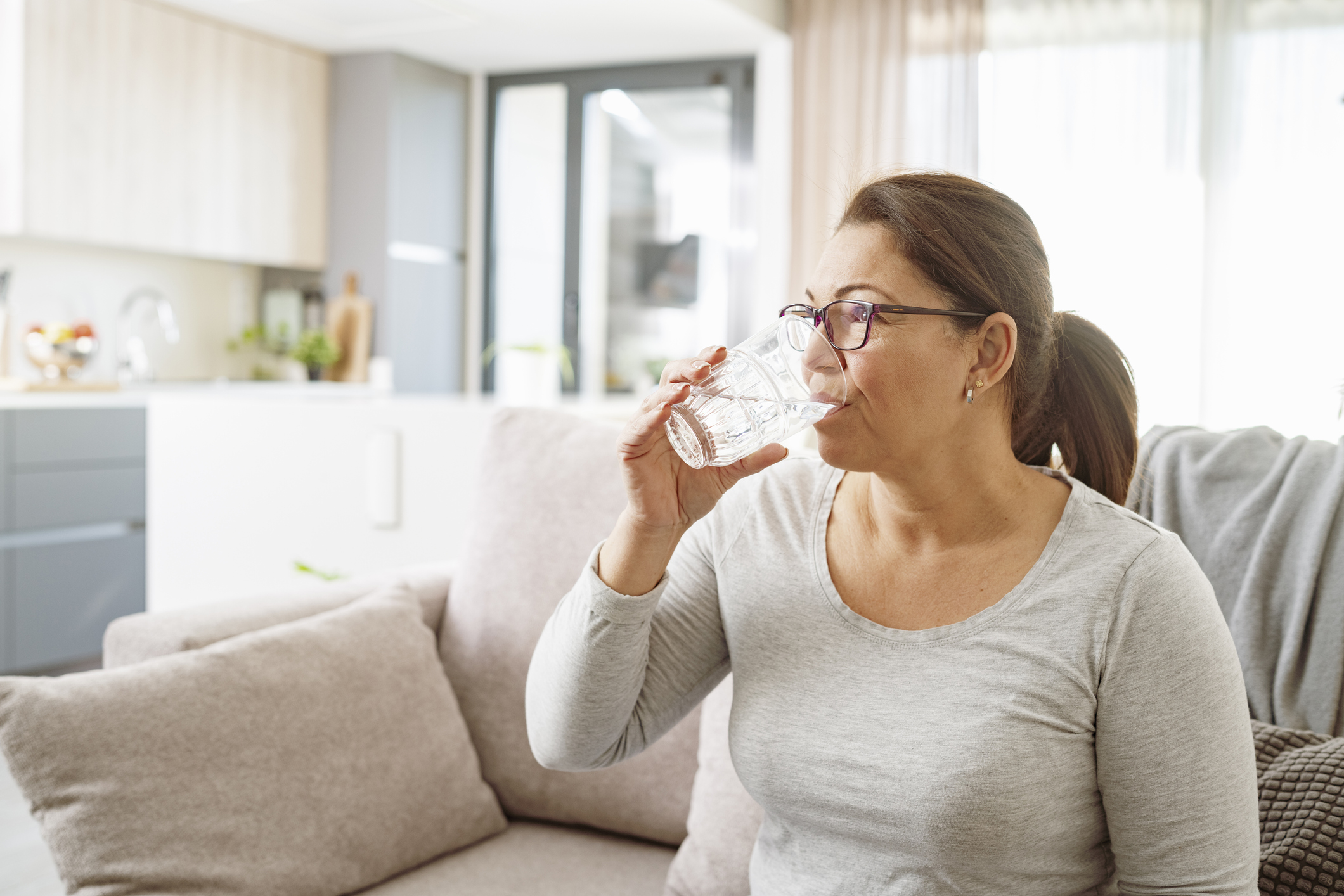 Vrouw zit op bank en neemt medicijn met glas water in
