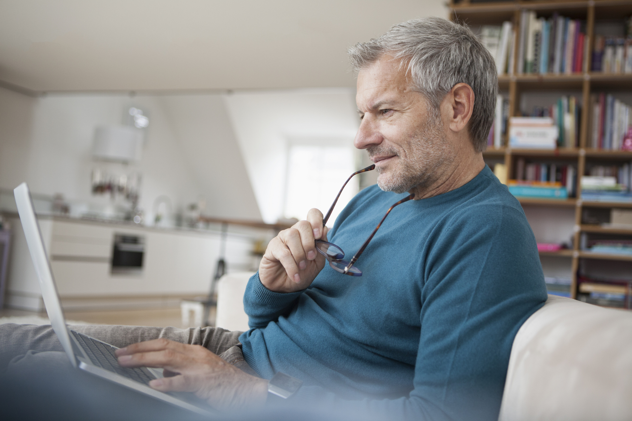 Oudere man checkt email op zijn laptop in de woonkamer met boekenkast