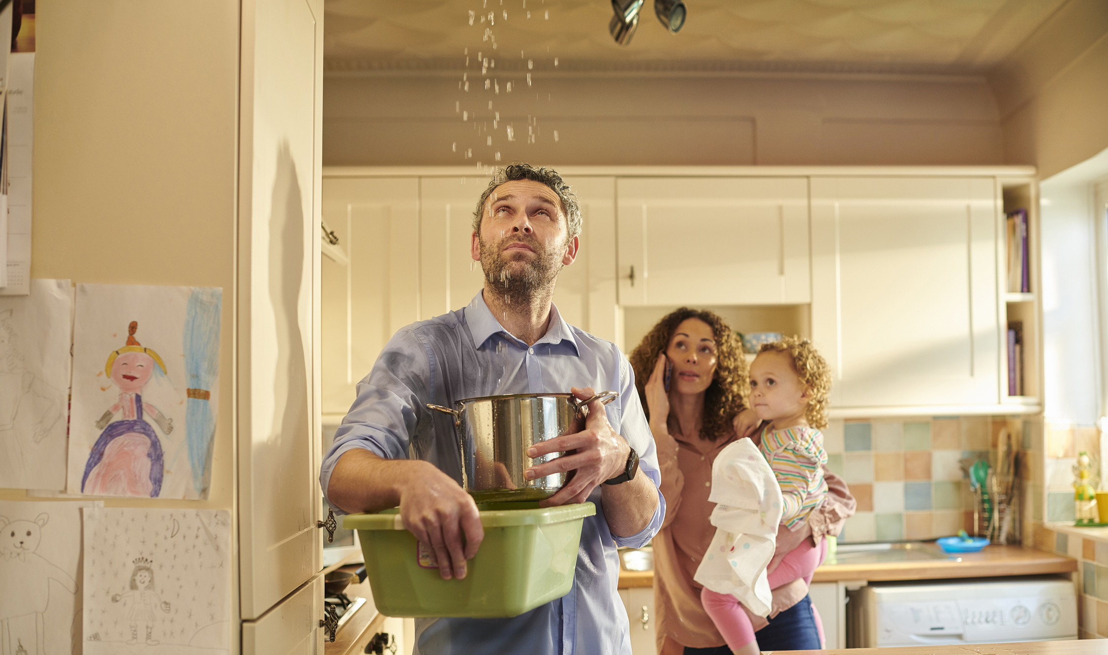 Lekkage in huis, vader met pan vol water en familie op de achtergrond