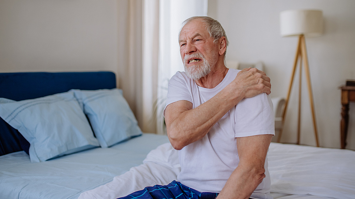 Man met zere schouders zittend op een bed