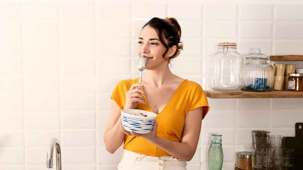 Vrouw zit op aanrecht yoghurt te eten