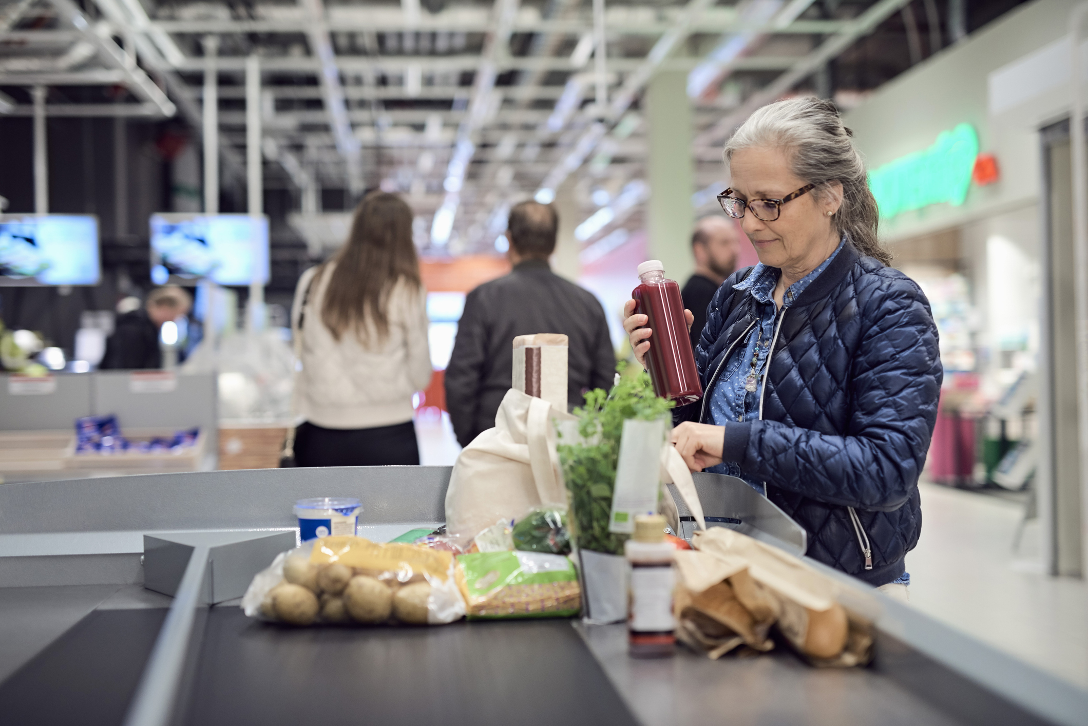 Mature woman keeping juice bottle in bag while standing at checkout counter