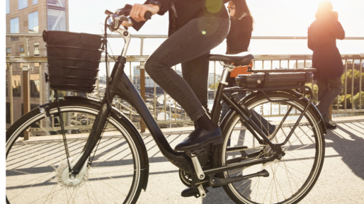 Low section of mature woman riding electric bicycle by commuters on bridge in city against sky