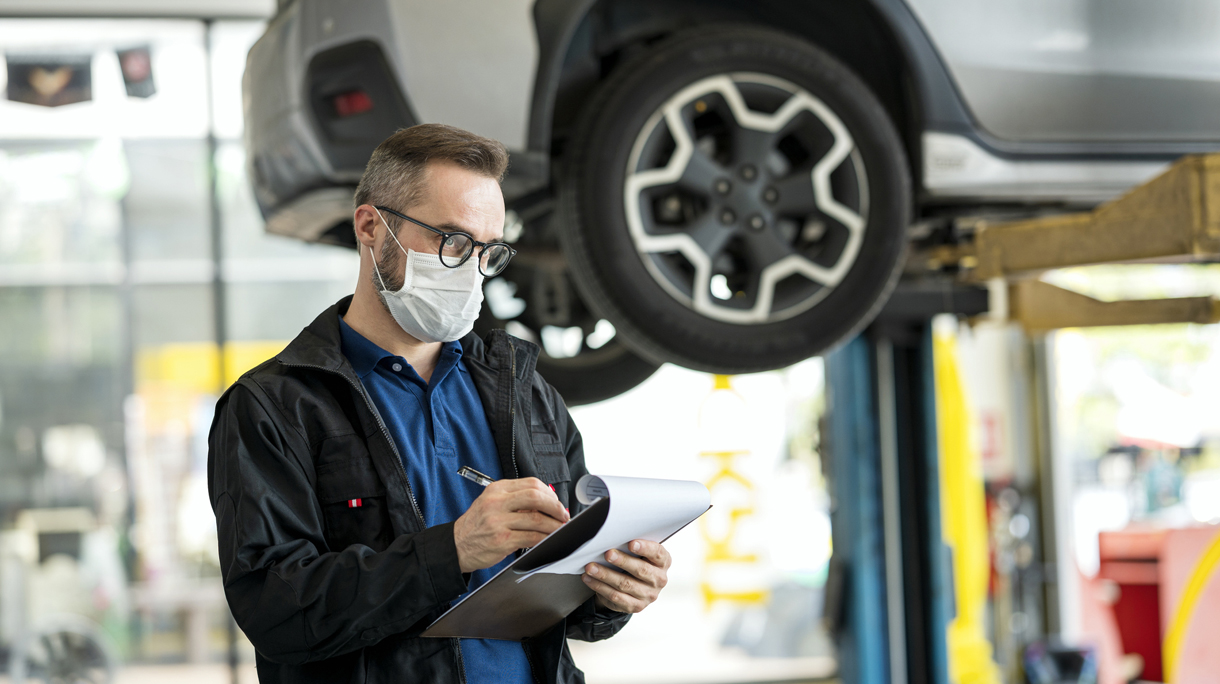 Male mechanic manager working with clipboard in car repair center. Car damage assessments and repairs process.