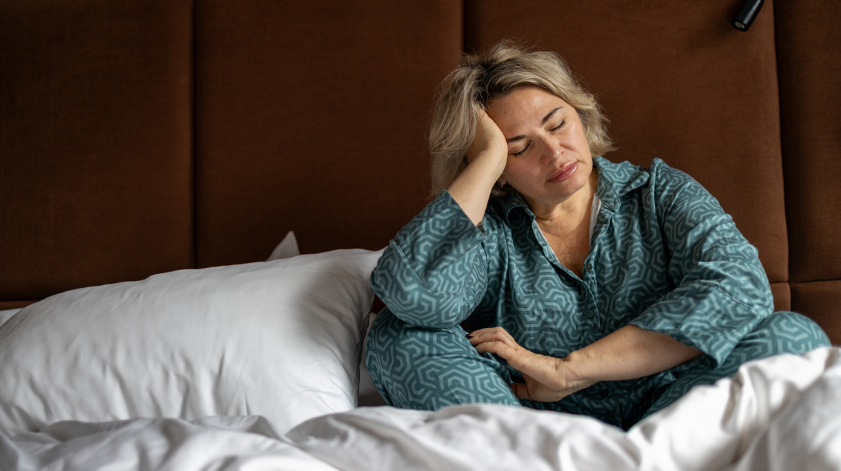 Vrouw zit uitgeput op bed met de handen in het haar