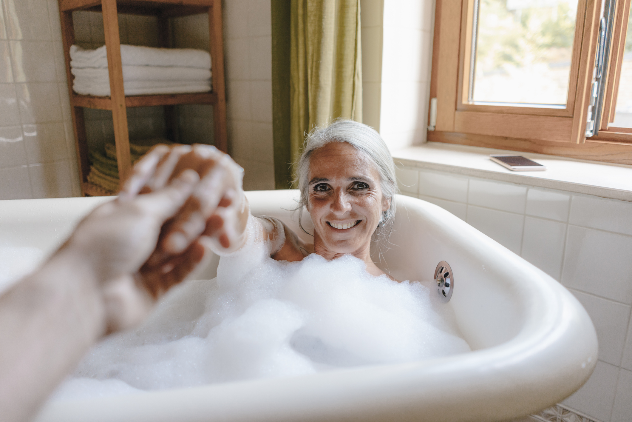 Vrouw in bad met bubbels, man houdt hand vast