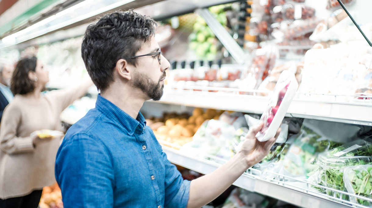 Man in supermarkt leest verpakking van product in het koelvak