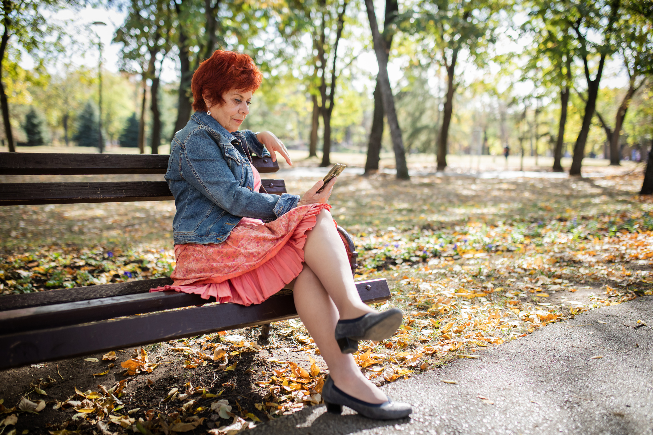 Vrouw met rok speelt met smartphone op een bank in een park met bomen