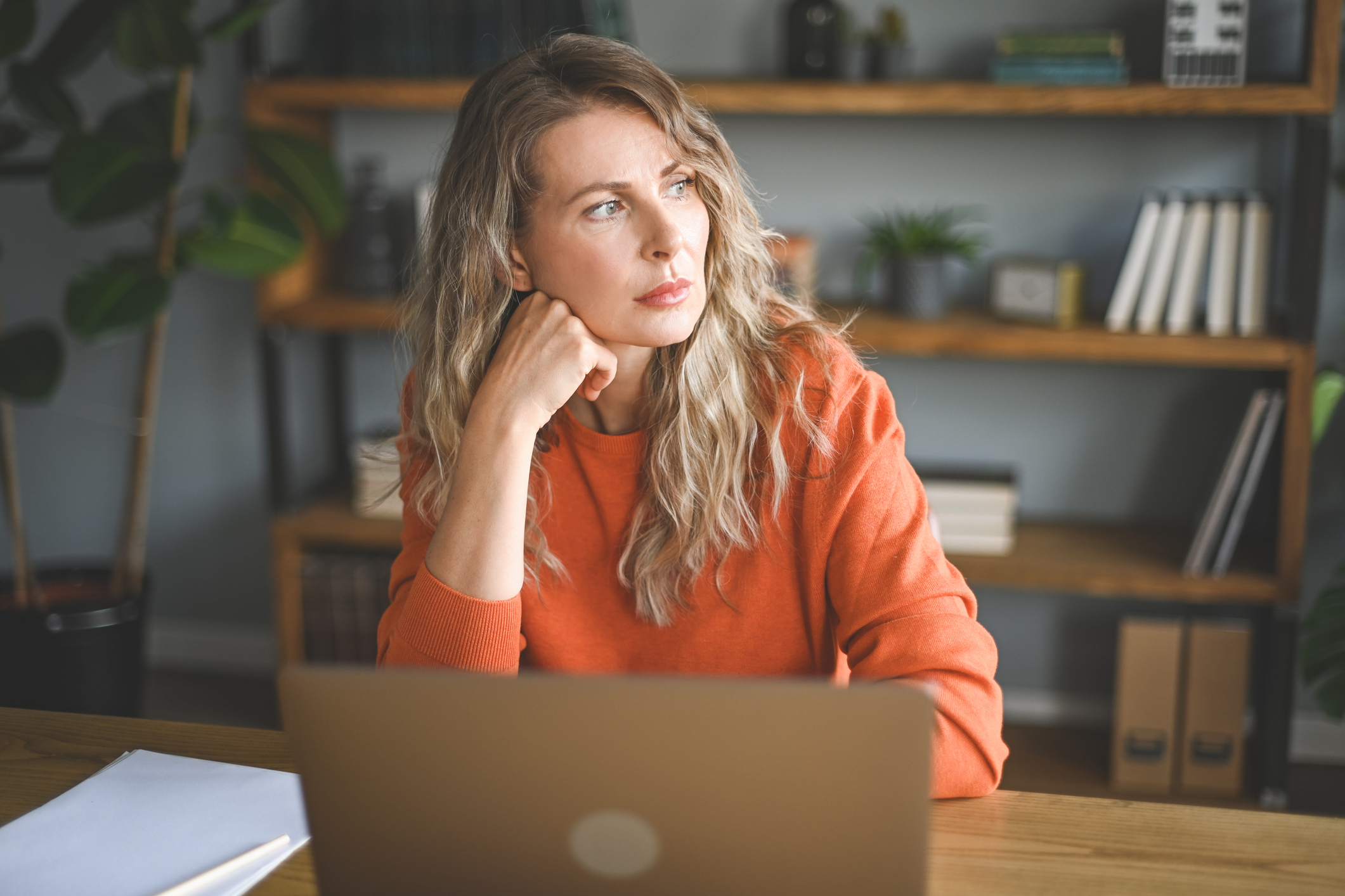 Vrouw van begin 40 kijkt bezorgd achter laptop in haar woonkamer