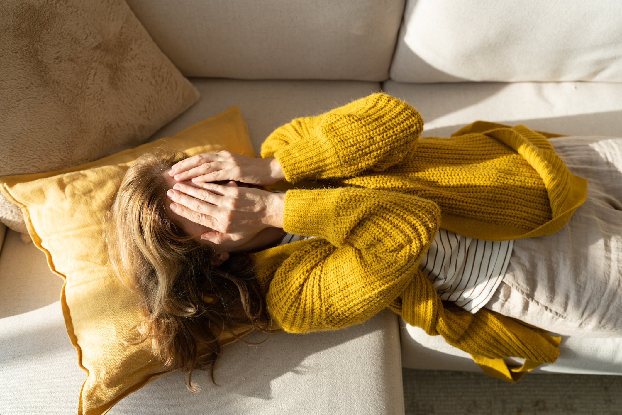 Vrouw ligt met handen voor haar ogen op de bank