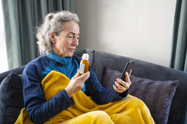 Vrouw zit met smartphone en fles medicatie op de bank