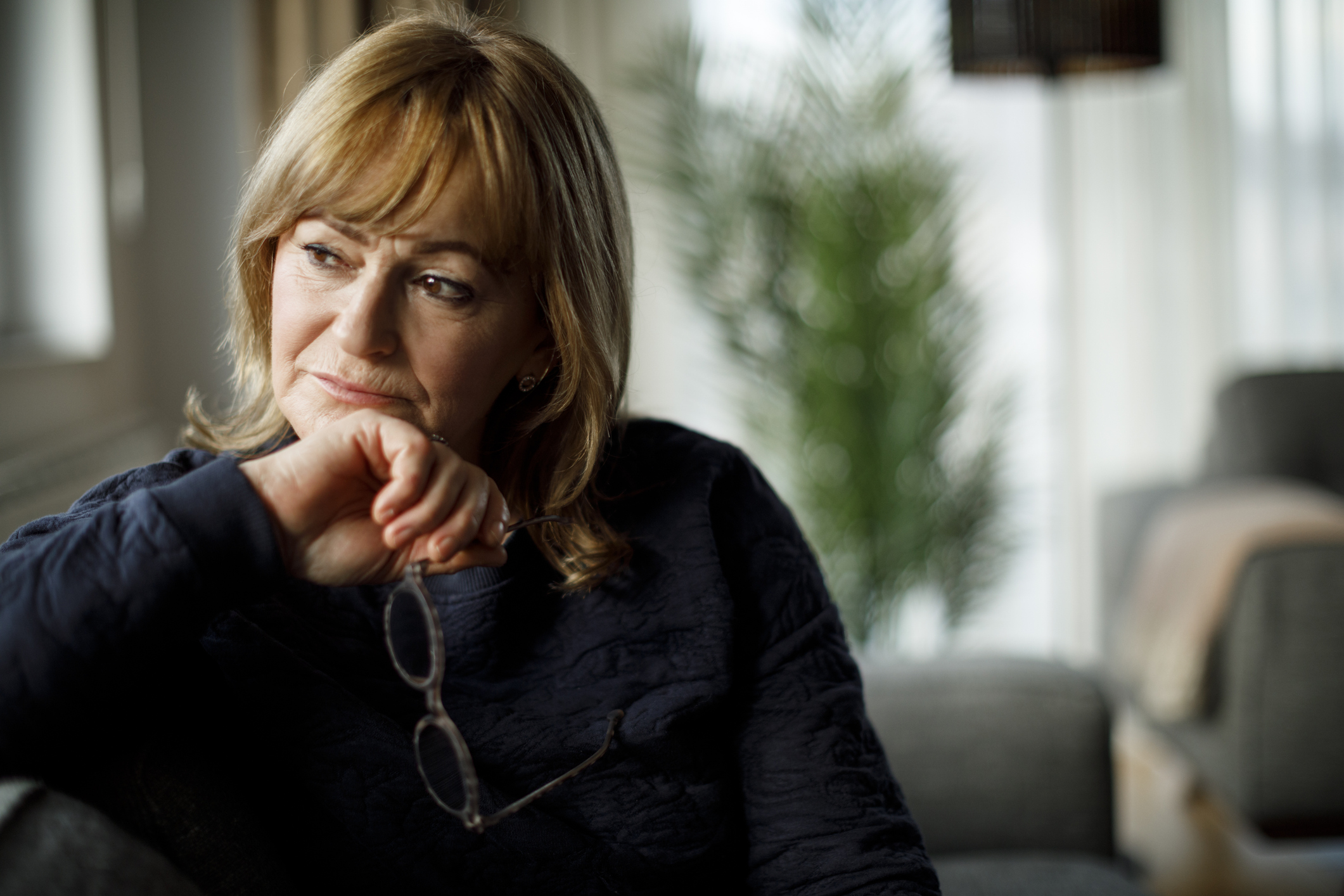 Oudere dame aan het peinzen op de bank, bril in haar hand