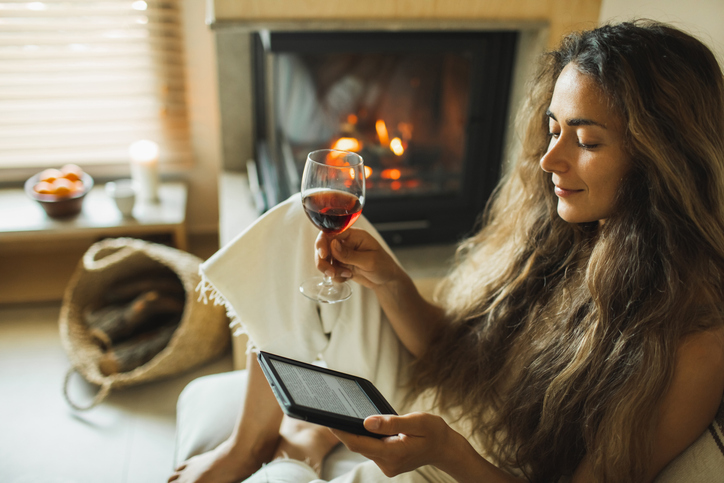 Knappe vrouw met lang haar leest uit e-reader met glas wijn in haar hand