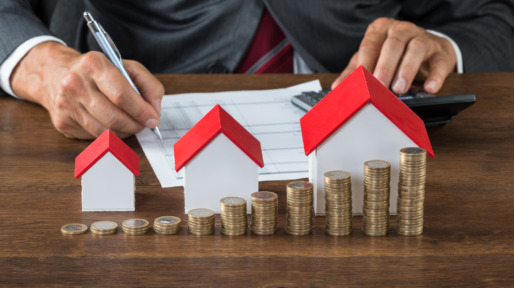 Businessman Calculating Tax By House Models And Coins