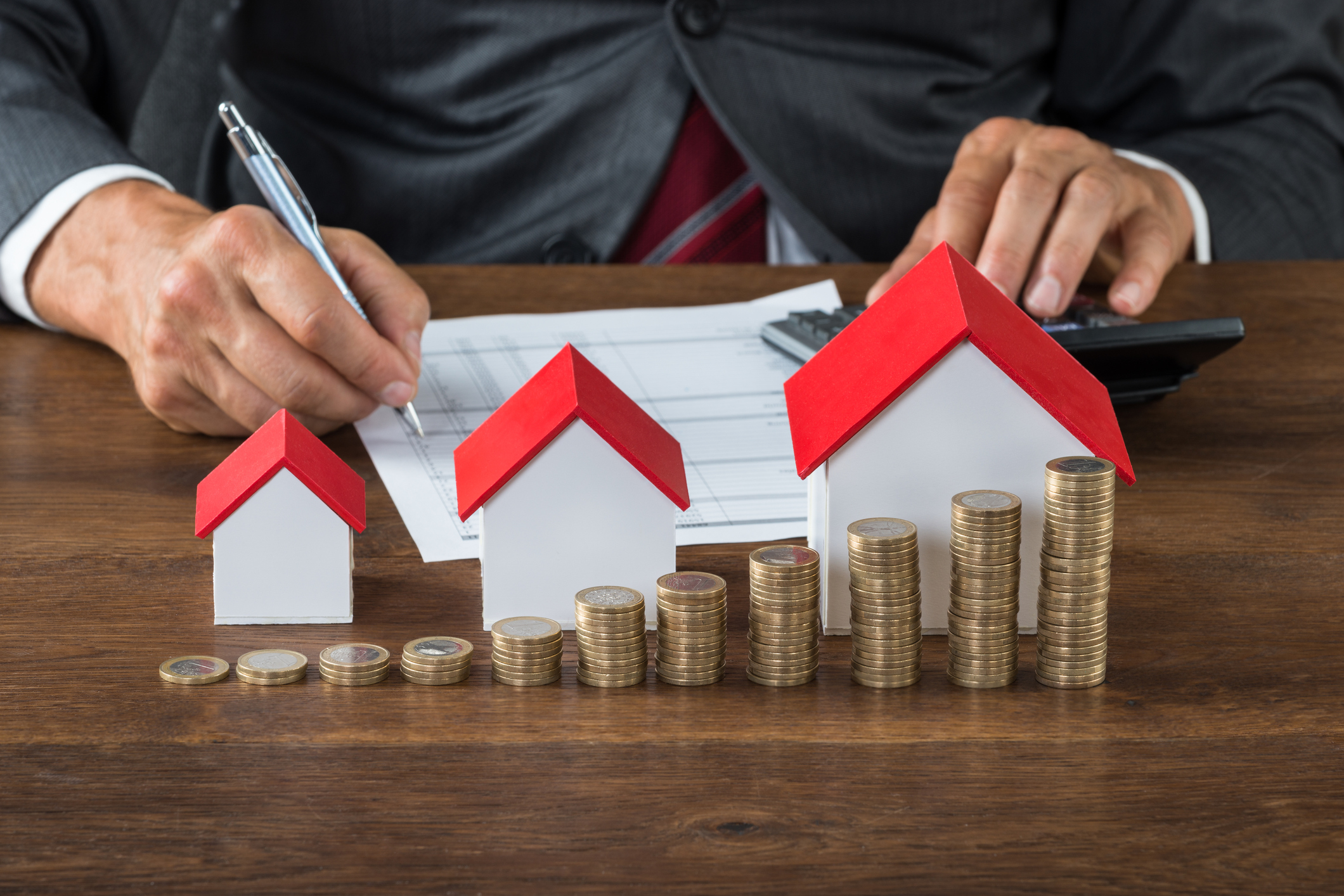 Businessman Calculating Tax By House Models And Coins
