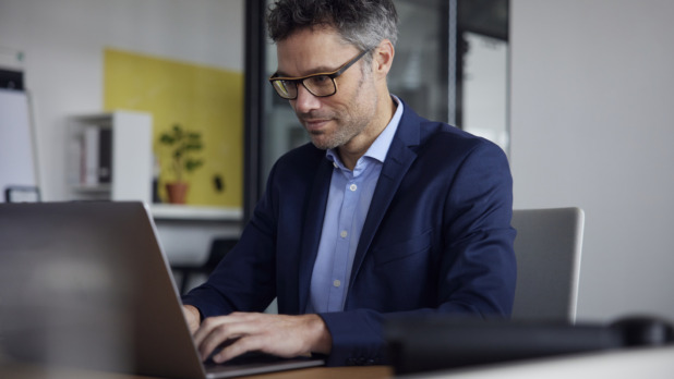 Oudere man met bril en colbert is hard aan het werk op zijn laptop