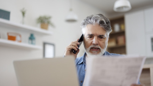 Man kijkt ernstig aan de telefoon met papier en computer in de kantoorkamer