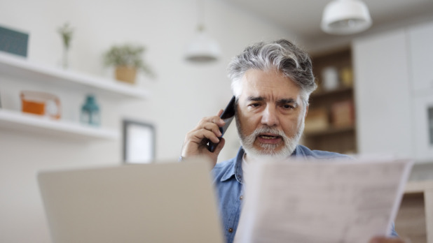 Man kijkt ernstig aan de telefoon met papier en computer in de kantoorkamer