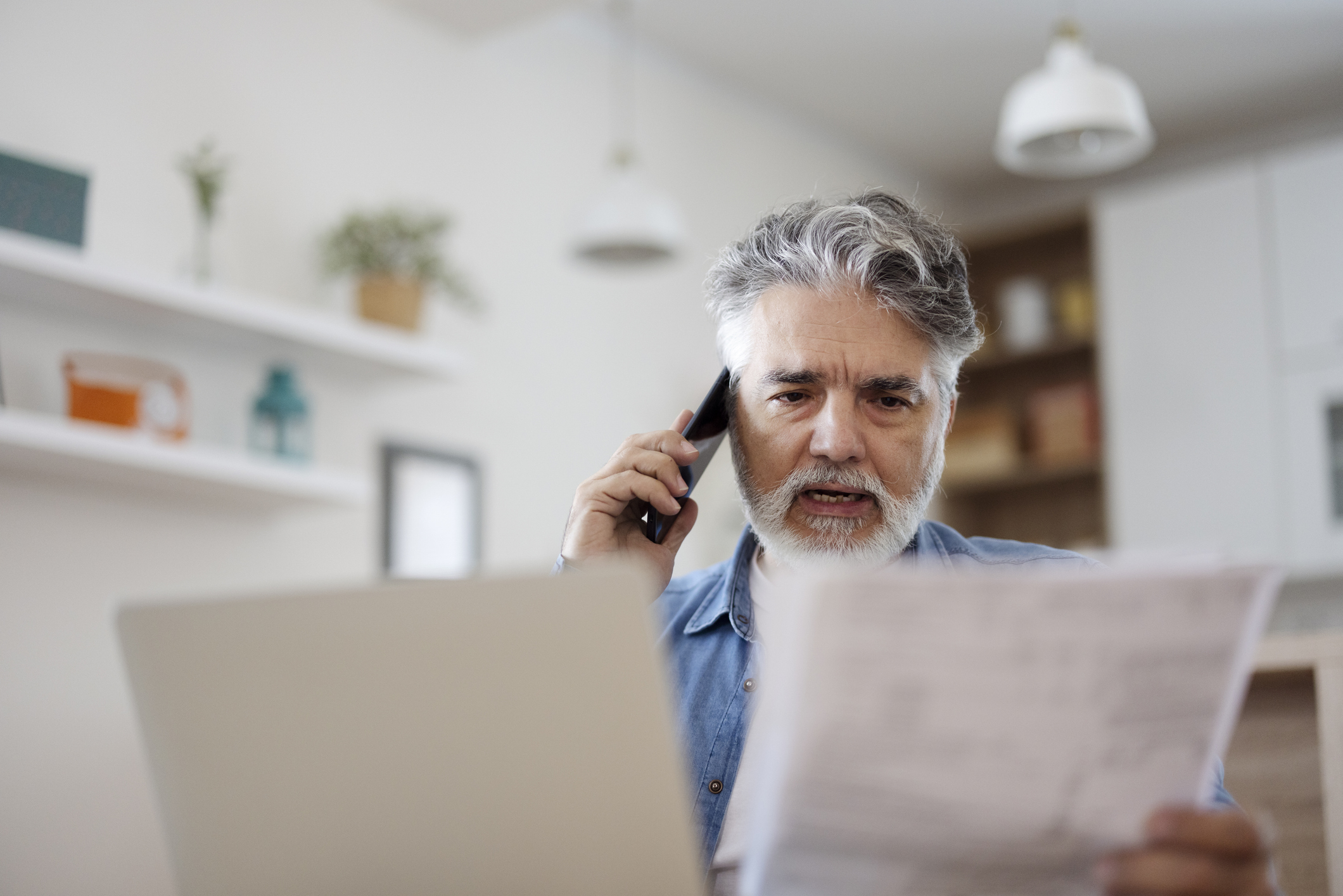 Man kijkt ernstig aan de telefoon met papier en computer in de kantoorkamer