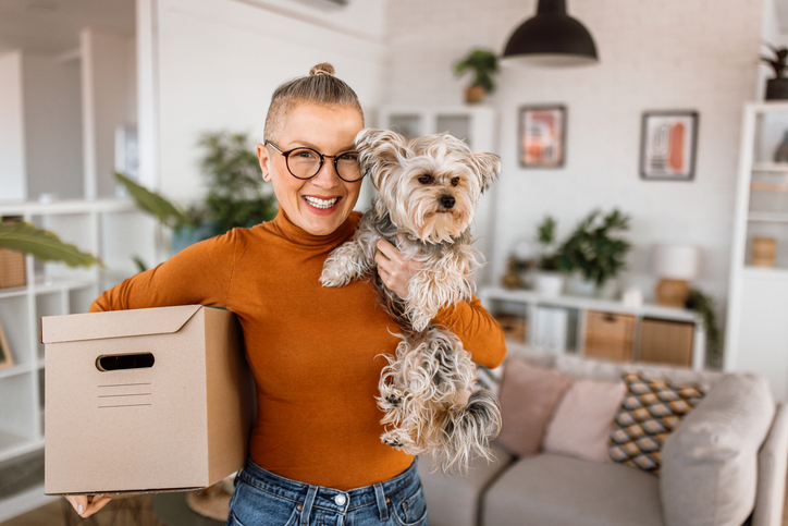 Vrouw met hond is bezig met verhuizen, doos in haar arm, hond in de andere