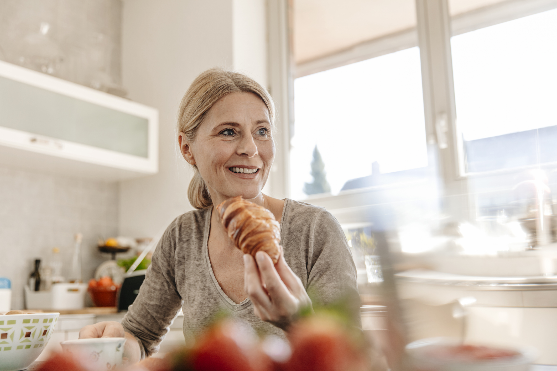 Vrouw eet roomboter croissant in de keuken, buiten schijnt de zon