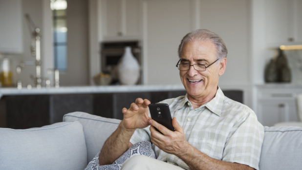 Man is vrolijk met telefoon bezig in huiskamer