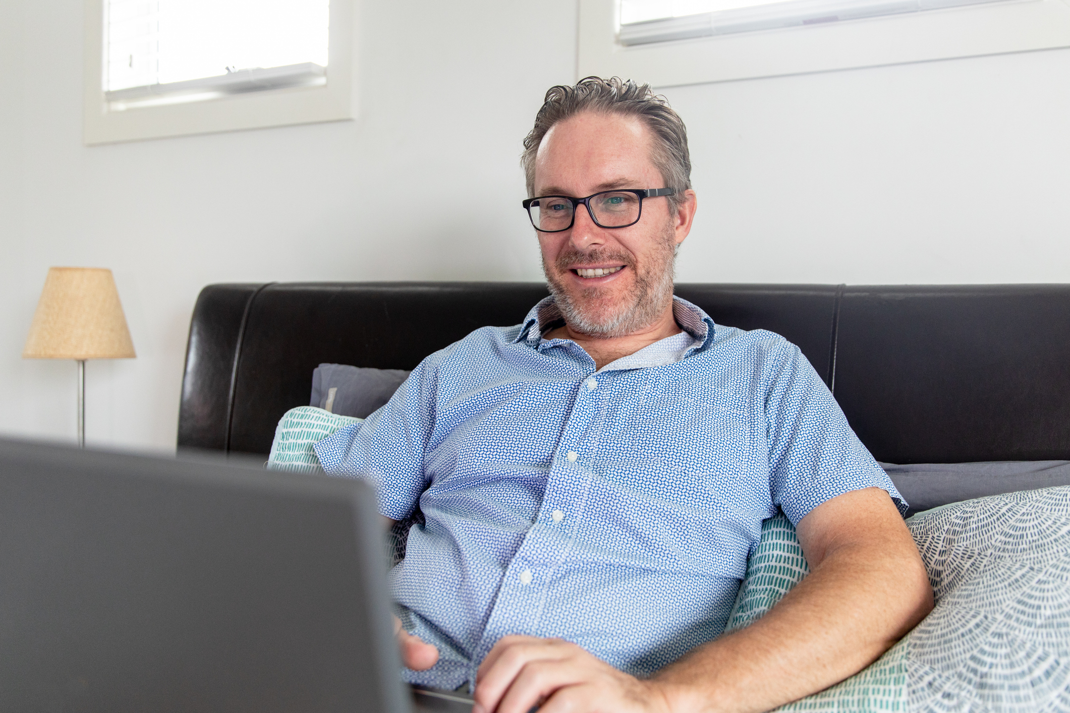 Man zit op de bank blij te spelen met zijn laptop