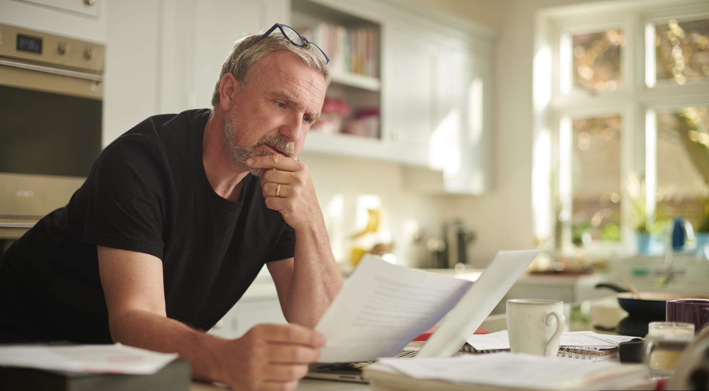Man is thuis zijn financien aan het bekijken, leunend op de tafel