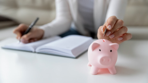 Vrouw schrijft haar uitgaven op en stopt geld in spaarvarken