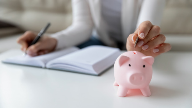 Vrouw schrijft haar uitgaven op en stopt geld in spaarvarken