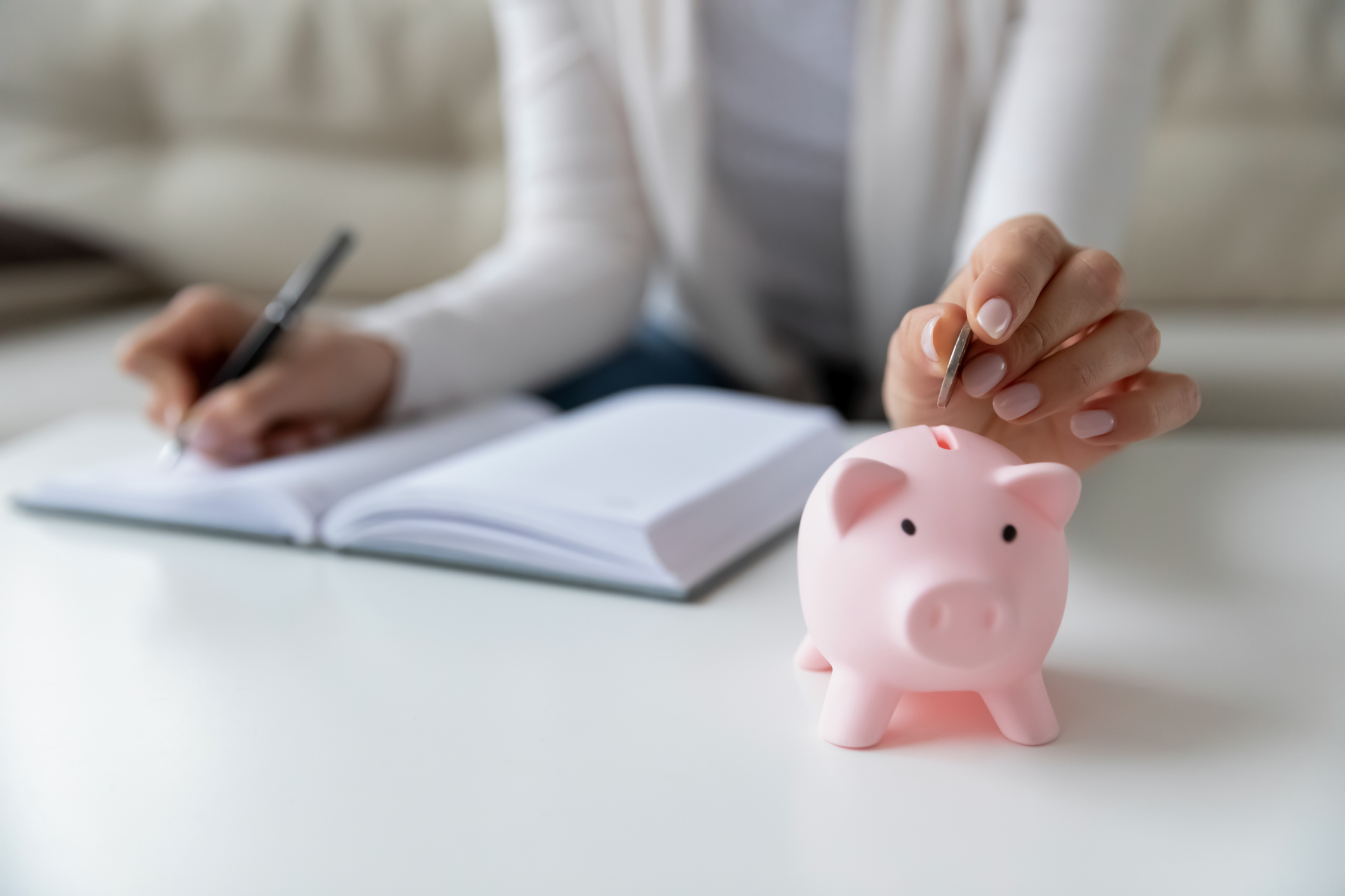 Vrouw schrijft haar uitgaven op en stopt geld in spaarvarken