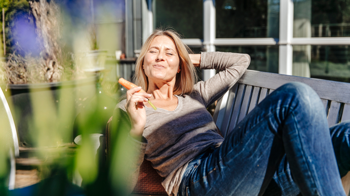 Vrouw zit buiten en eet een wortel