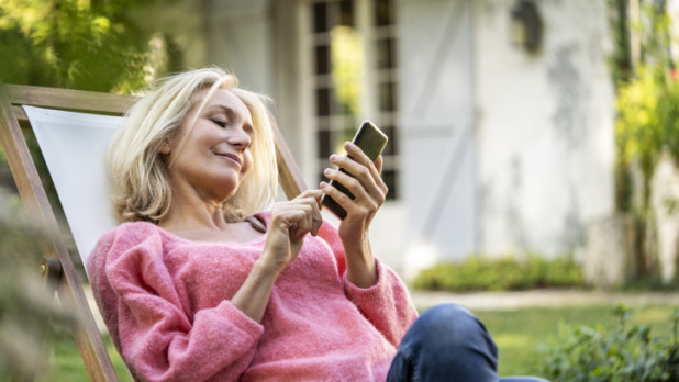 Vrouw zit in tuinstoel met haar smartphone te spelen