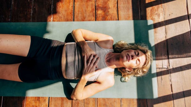 vrouw doet ademhalingsoefeningen op yogamat